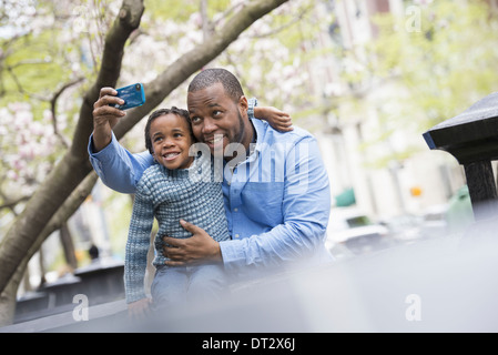 New York city park spring Sunshine and cherry blossom A father and son side by side Using a smart phone to take a picture Stock Photo