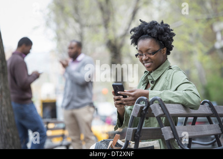 A woman on a bench checking her phone Two men in the background Stock Photo