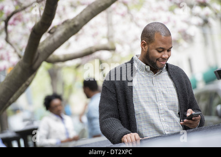 A young man checking his phone and texting A couple in the background Stock Photo