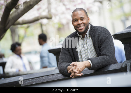 A man seated at a table and two people in the background Stock Photo