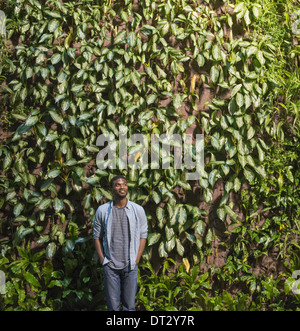 A man looking up at a high wall covered in climbing plants and foliage Stock Photo