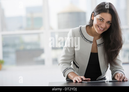 Young professionals at work A woman at a work table using a digital tablet Looking up and smiling Stock Photo