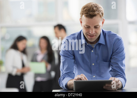 Young professionals at work A man in an open necked shirt using a digital tablet in the background Stock Photo