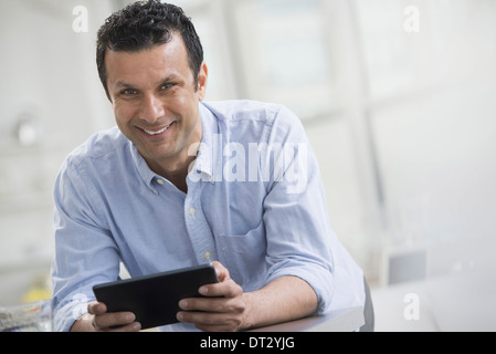 A man in a blue shirt leaning on a desk holding a digital tablet Stock Photo