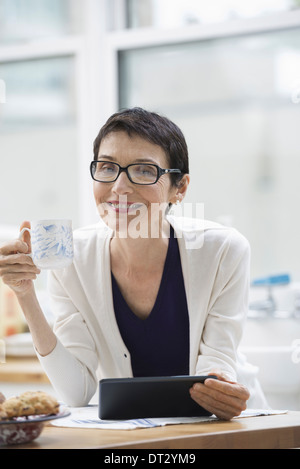 New York City A woman dressed for work in cream jacket holding a cup of coffee Checking her digital tablet Stock Photo