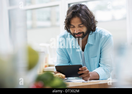 An office or apartment interior in New York City A bearded man in a turquoise shirt using a digital tablet Stock Photo