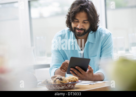 An office or apartment interior in New York City A bearded man in a turquoise shirt using a digital tablet Stock Photo
