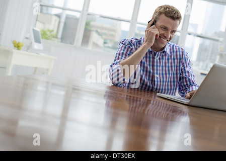 A man using the phone and typing on his laptop Stock Photo