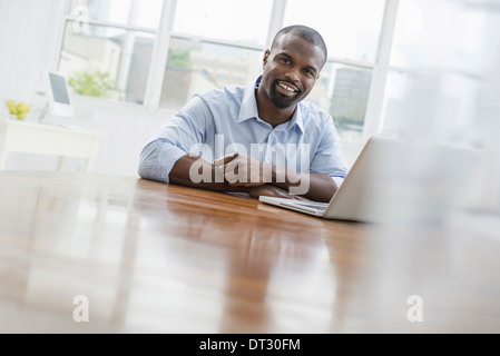 An office or apartment interior in New York City A man seated at a table using a laptop computer Stock Photo