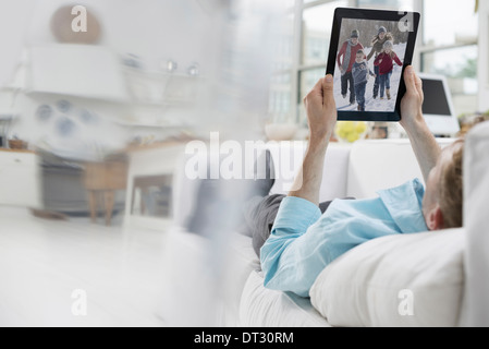 A man lying on a sofa in comfort in a quiet airy office environment Using a digital tablet Stock Photo