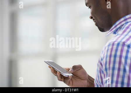 Professionals in the office A light and airy place of work A man in a checked shirt using a smart phone Stock Photo