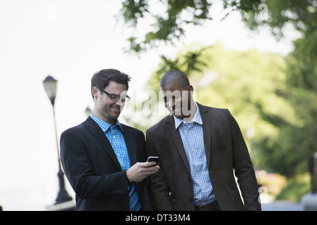 Two men walking side by side one showing the other his smart phone Stock Photo