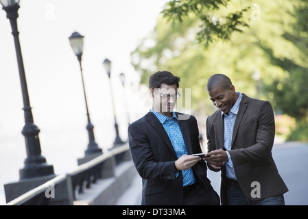 Two men walking side by side one showing the other his smart phone Stock Photo
