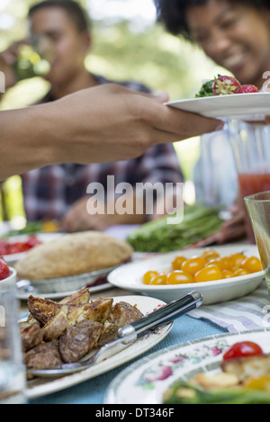 A family picnic in a shady woodland Adults and children sitting at a table Stock Photo