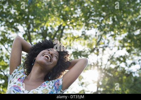 A young woman in a flowered summer dress with her hands behind her head smiling and looking up Stock Photo