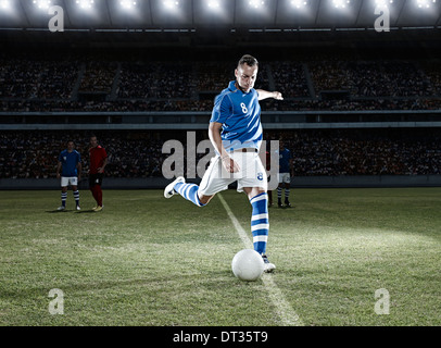 Soccer player kicking ball on field Stock Photo
