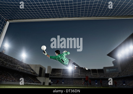 Goalie jumping for ball in soccer net Stock Photo