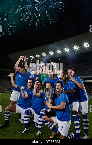 Soccer team cheering with trophy on field Stock Photo