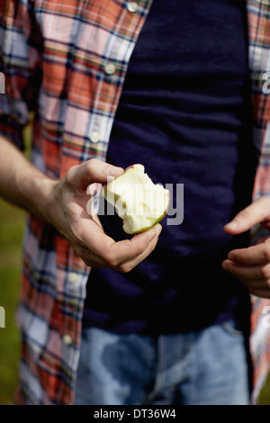 Mid section of a man wearing a plaid shirt holding a half eaten apple Stock Photo