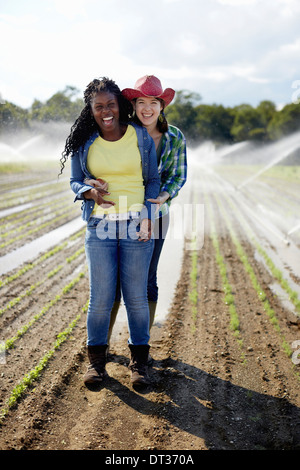 Two young women standing in a field of small seedlings with the irrigation sprinklers spraying the ground Stock Photo