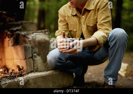 A man kneeling by a blazing camp fire Stock Photo