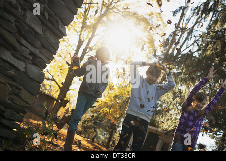 Three children in the autumn sunshine. Playing outdoors throwing the fallen leaves  in the air. Stock Photo