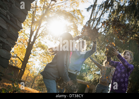 Three children in the autumn sunshine. Playing outdoors throwing the fallen leaves  in the air. Stock Photo