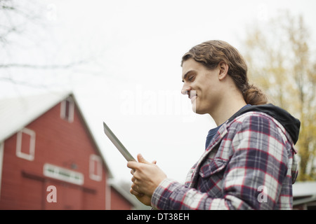 A young man using a computer tablet, a portable PC tablet device, on an organic farm. Stock Photo