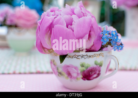 Pink peony and forget-me-nots in a vintage teacup and out of focus teacup with roses in background Stock Photo