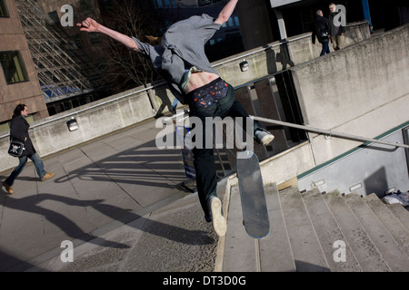 Pedestrians ignore a young skateboarder flying through the air during his acrobatic jump down steps. Stock Photo