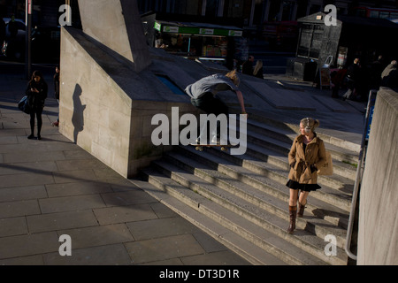 Young women unaware of young skateboarder suddenly flying through air during his acrobatic jump over steps. Stock Photo