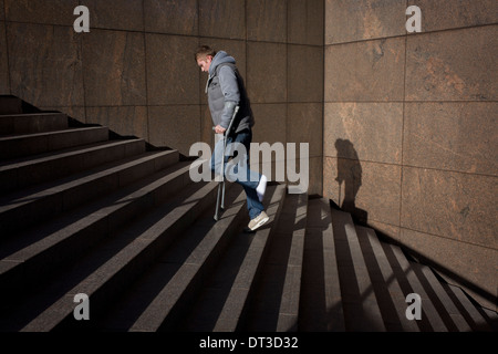 Young man hobbles up steep steps, hopping on one foot with the aide of crutches. Stock Photo