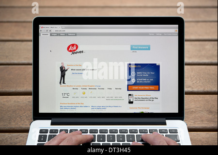 The Ask Jeeves website on a MacBook against a wooden bench outdoor background including a man's fingers (Editorial use only). Stock Photo