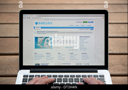 The Barclays website on a MacBook against a wooden bench outdoor background including a man's fingers (Editorial use only). Stock Photo