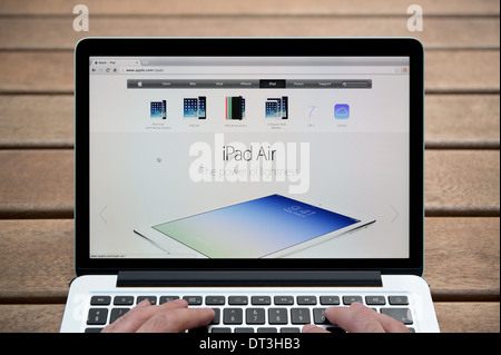 The Apple iPad website on a MacBook against a wooden bench outdoor background including a man's fingers (Editorial use only). Stock Photo