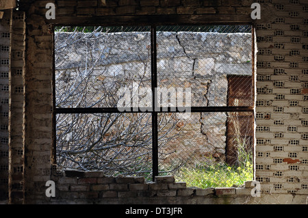 View to overgrown garden through threaded window. Abandoned interior. Stock Photo