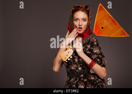 Girl in Russian style posing in red kerchief and bagels on the neck. Holding a balalaika. Stock Photo