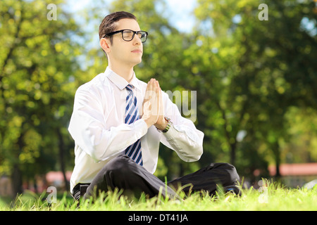 Young businessman doing yoga exercise seated on a grass in a park Stock Photo
