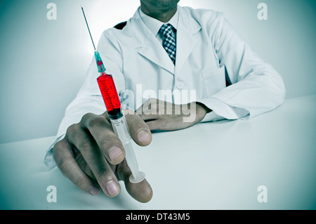 a sinister doctor sitting in a desk holding a syringe Stock Photo