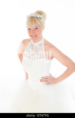 A blonde bride in a wedding dress and tiara with her hands on smiles while looking at the camera Stock Photo