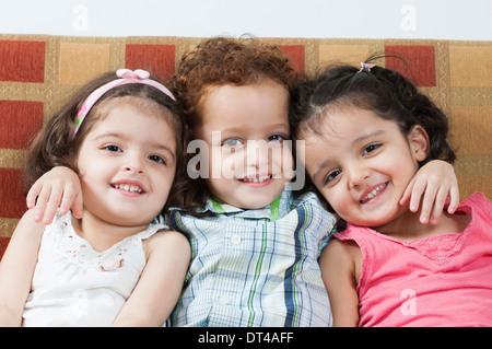 3 years old triplets sat on sofa Stock Photo