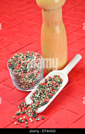Mixed peppercorns in a glass and in a scoop on a red textile. Pink, black, green and white pepper Stock Photo