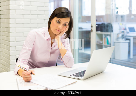 Tired businesswoman at desk working with computer and paper Stock Photo