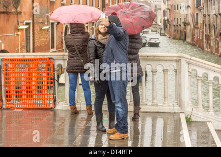 Venice, Italy. Young couple in winter and rain clothing taking pictures of themselfs at a rainy day on a bridge over a canal. Stock Photo
