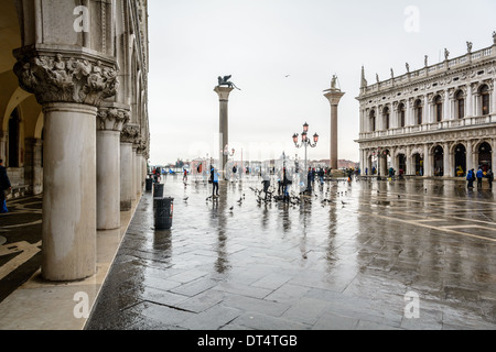 Venice, Italy. View over the Piazzetta di San Marco with two columns and tourists in rainwear feeding pigeons on a rainy day. Stock Photo