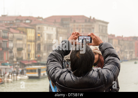 Venice, Italy. View over the Grand Canal through the display of a smartphone from a man taking pictures from an Asian couple. Stock Photo