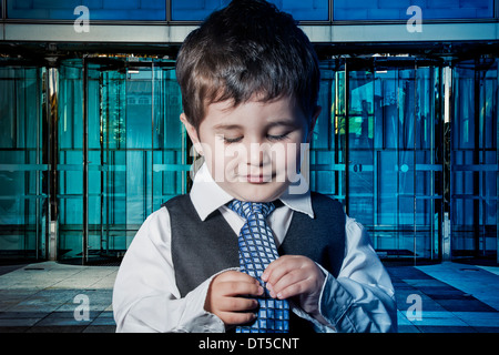 Success child dressed businessman with hands in his tie and skyscrapers in the background Stock Photo