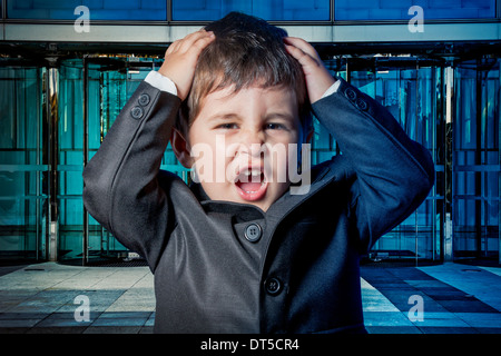 Serious child dressed businessman with hands in his tie and skyscrapers in the background Stock Photo