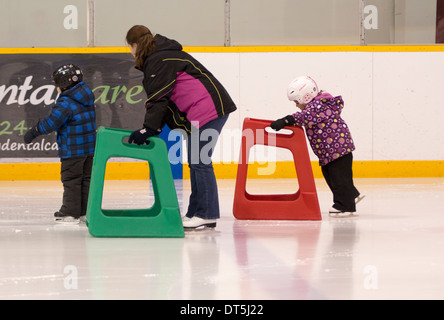 Mother, son and daughter learning to ice skate with assistance in indoor skating rink Stock Photo