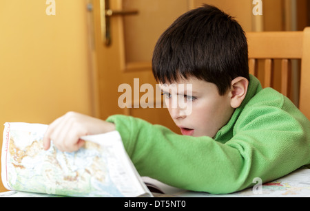 bored and tired boy doing homework from school in workbook using worl map Stock Photo